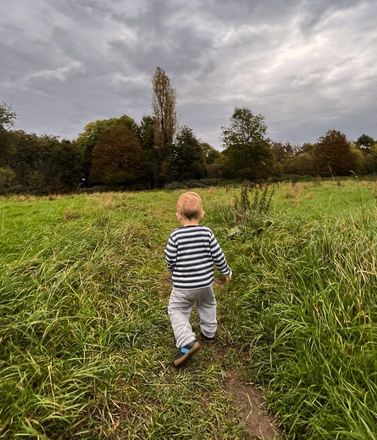 Kleinkind im gestreiften Pullover läuft allein über eine weite Wiese am Kinderbauernhof Neuss