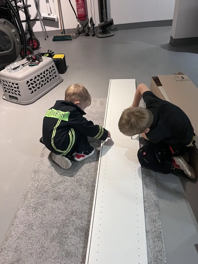 Zwei Kinder hocken auf dem Boden einer Halle und spielen