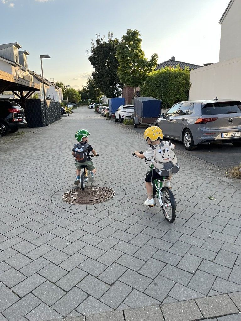 Zwei Kinder fahren mit Laufrad und Fahrrad über eine ruhige Wohnstraße
