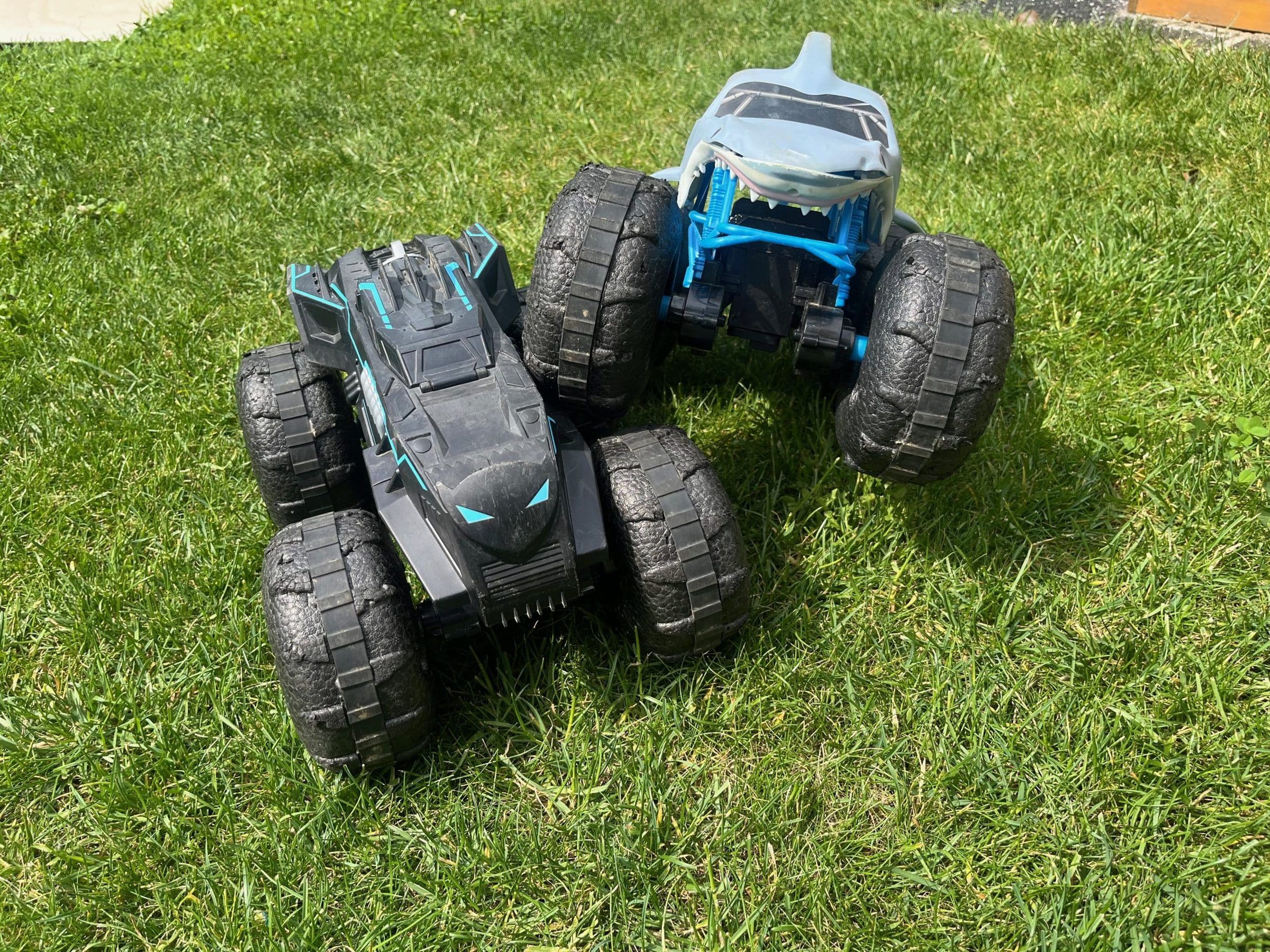 Zwei ferngesteuerte Monstertrucks im Batman- und Hai-Design auf dem Rasen